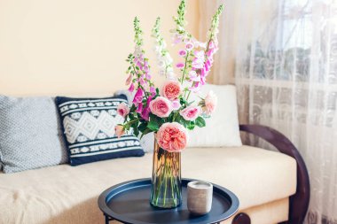 Oturma odasındaki vazoya taze bir buket gül ve tilki eldiveni koyduk. Ev ve iç dekorasyon. Masada pembe turuncu çiçekler var.