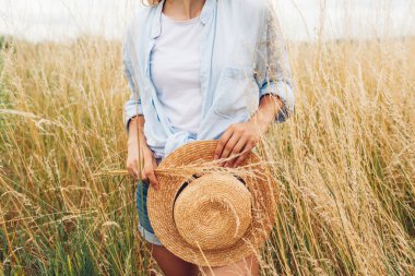 Yaz için kadın aksesuarlarını ve kıyafetlerini kapatın. Çayırda keten gömlek giyen hasır şapkalı bir kadın. Doğal hipoalerjenik kıyafetler.