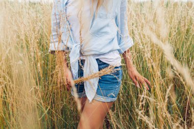Young woman walking in meadow picking grasses wearing linen shirt and jeans shirts. Natural summer clothes. Comfortable fabric