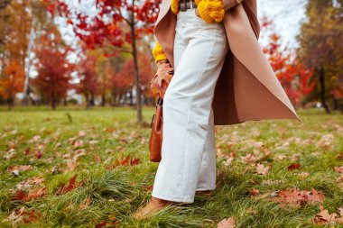 Close up of stylish white flared pants. Woman walking in fall park wearing warm fashionable clothes. Autumn outfit in white beige orange colours.