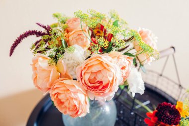 Fresh bouquet of roses zinnia amaranth flowers put in vase on table. Process of arranging with basket and pruner. Home decor. Close up