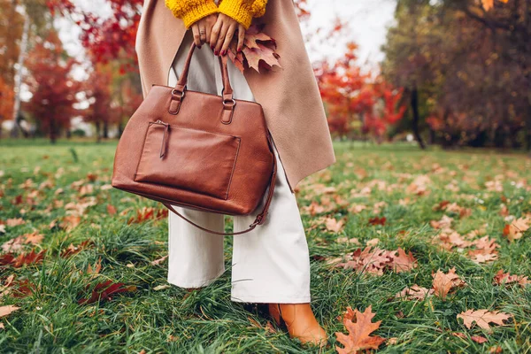 秋の公園でコートやフレアパンツを身に着けている女性が保持するスタイリッシュな革ハンドバッグの閉鎖 秋の女性の服 アクセサリー ファッショナブルな外観 — ストック写真