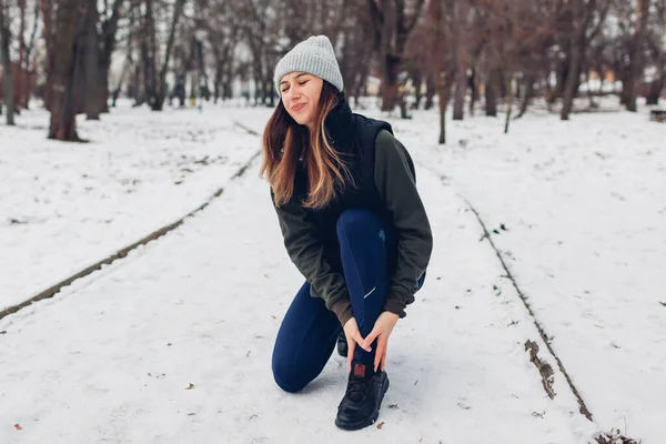 在雪地的冬季公园进行训练时 跑步者的腿受了伤 女人觉得受伤脚踝疼痛寒冷天气下在室外进行危险的锻炼 — 图库照片