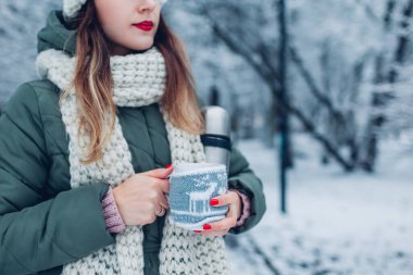 Kış parkında, örgü Noel kutusuna bürünmüş bir fincan çay ya da kahveyi yakın. Soğuk ve karlı havada ısınmak için içecekler.