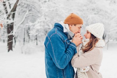 Soğuk kış parkında nefesiyle kadını ısıtan adam. Sevgi dolu çift soğuk havada dışarıda yürüyor.