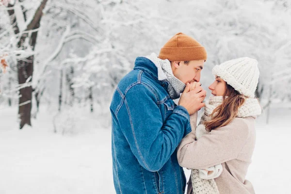 男人在雪地寒冷的冬季公园里用呼吸温暖着女人的手 多情的夫妻在寒冷的天气外出散步 — 图库照片