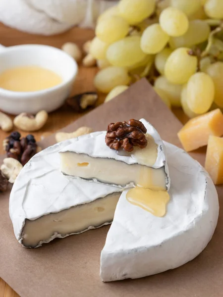 Brie-Käse mit Nüssen, Honig und Trauben auf Papier — Stockfoto