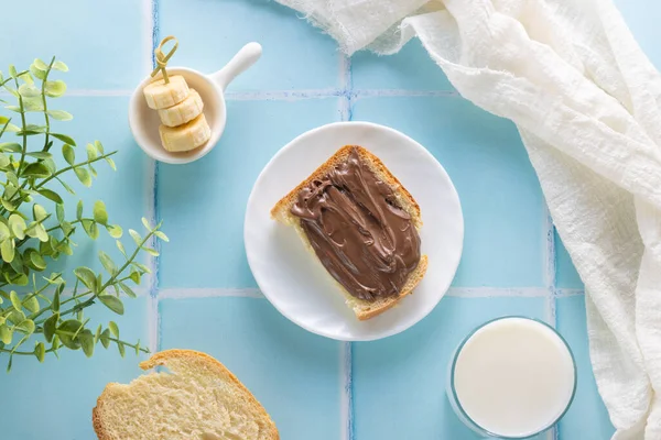 a sandwich with chocolate paste, milk and banana on a blue tile background