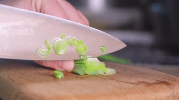 Жіноча рука розрізає зелену цибулю ножем на дерев'яній дошці — стокове відео