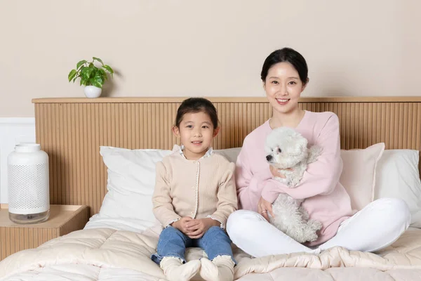 アジア系韓国人の母親と娘と子犬犬はベッドの上に座って — ストック写真
