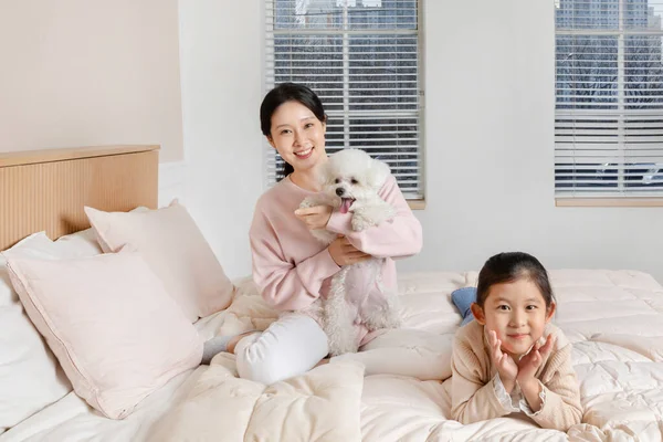 アジア系韓国人の母親と娘と子犬犬はベッドの上に座って — ストック写真