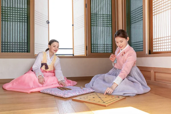 Korean and Caucasian girls wearing Hanbok playing Yut, Korean traditional board game