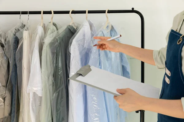 aesthetic laundry concept_person checking the rack with clean shirts in plastic bags after dry cleaning