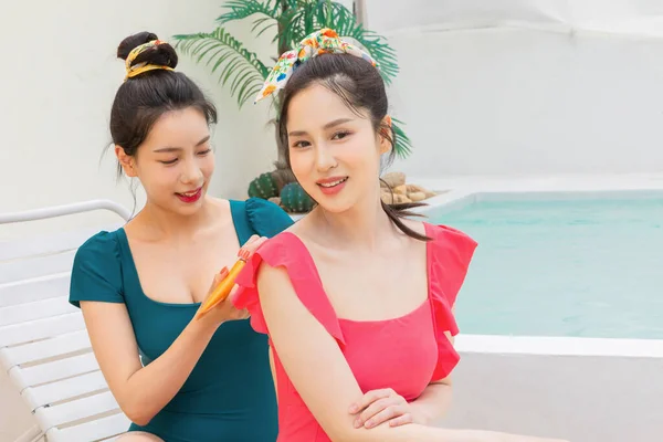 Две Корейские Красивые Молодые Женщины Применяют Крем Загара Возле Бассейна — стоковое фото