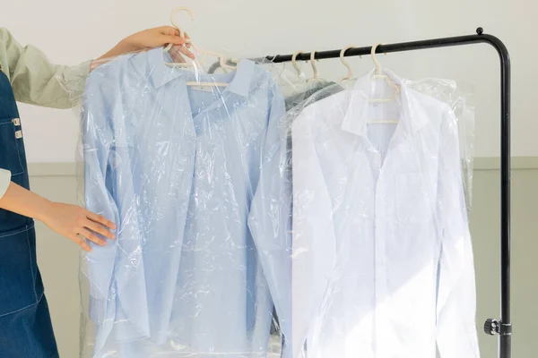 aesthetic laundry concept_person checking the rack with clean shirts in plastic bags after dry cleaning