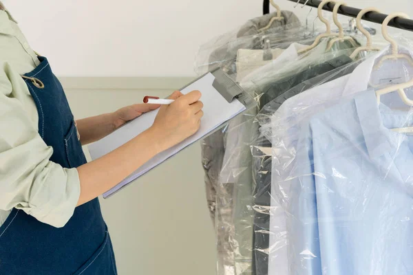 aesthetic laundry concept_person checking the rack with clean shirts in plastic bags after dry cleaning