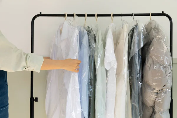 aesthetic laundry concept_person checking the rack with clean shirts in plastic bags after dry cleaning