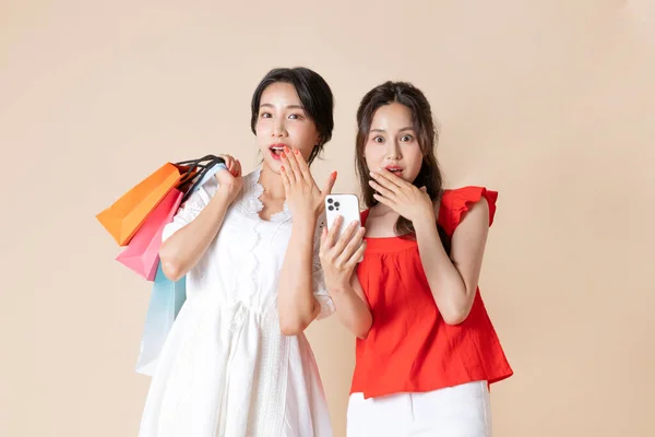 两个漂亮的韩国年轻女子拿着智能手机 手里拿着购物袋 — 图库照片