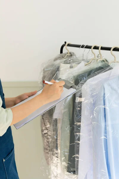 aesthetic laundry concept_person checking the rack with clean shirts in plastic bags after dry cleaning