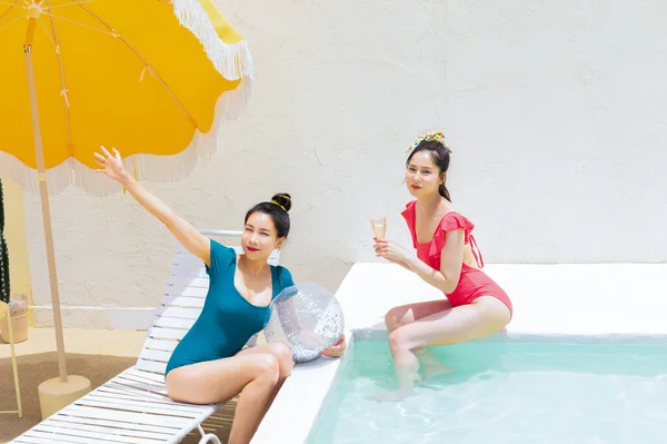 膨脹可能なボールとカクテルドリンクを持つスイミングプールで2人の韓国の美しい若い女性 黄色の傘の下に座って — ストック写真