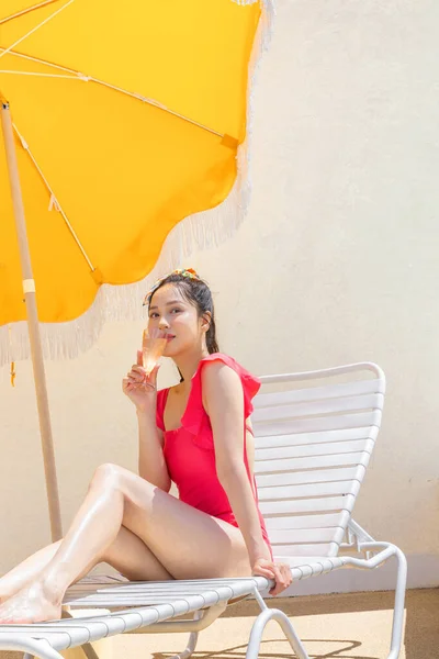 赤い水着を着用し サンラウンジャーでリラックスした韓国の美しいアジアの若い女性は ガラスから飲み物を楽しんで — ストック写真