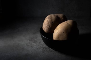 Siyah kabın içinde bir çift taze çiğ patatesli siyah yiyecek sahnesi..