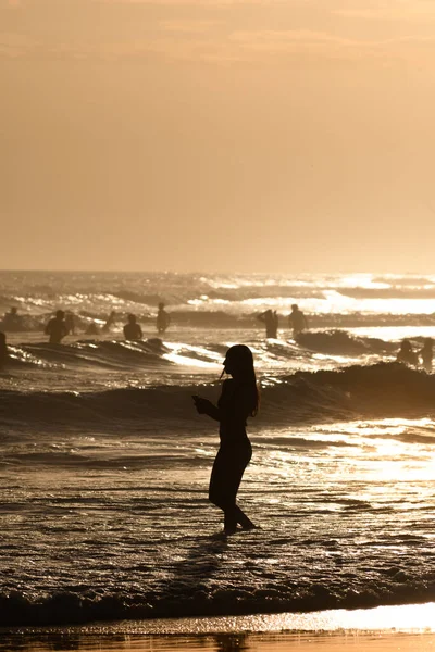 夕阳西下海滩上一个女人和其他背景中的人的轮廓 — 图库照片