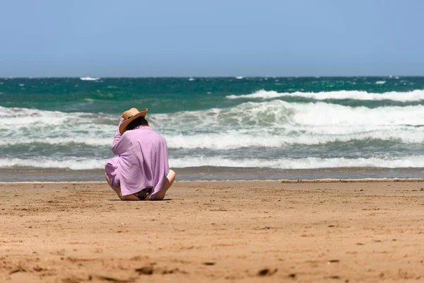 一个戴帽子的女人坐在沙滩上凝视着大海 — 图库照片