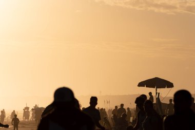Gün batımında sahilde insan siluetleri.