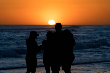 Sahilde renkli bir gün batımının önündeki insanların siluetleri..