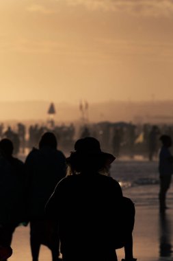Gün batımında sahilde insan siluetleri.