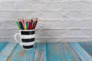 Renkli kalemlerle dolu çizgili bir kupa. Arka planda fotokopi alanı var..