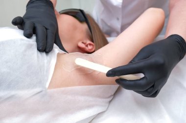 Genç bir kız için lazer tüyü çıkarma. Uzman, vücuttan lazer tüy çıkarma prosedürünü uygular.