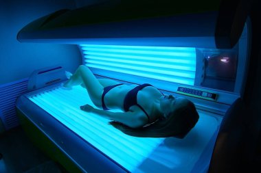 Kız solaryumda güneşleniyor..