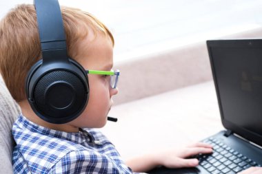 Kulaklıklı bir çocuk kanepede oturmuş bilgisayarcılık oynuyor.