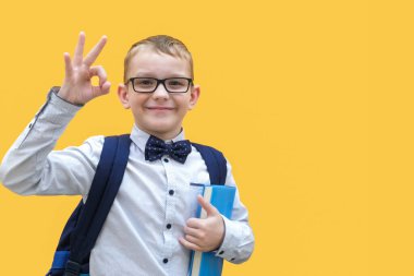 Gözlüklü ve okul çantalı mutlu bir çocuk elinde bir kitap tutuyor..