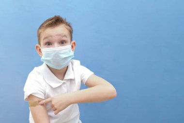 Mavi arka planda koruyucu maskeli bir çocuk. Çocuğa hastalık, koronavirüs ya da covid-19 aşısı yapıldı.