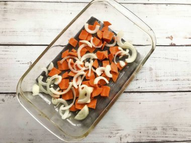 Soğanı soy ve yarım halkaları kes. Havuçları iyice yıka, soy ve küçük parçalara böl. Sebzeleri sebze yağıyla yağlanmış fırına koy..