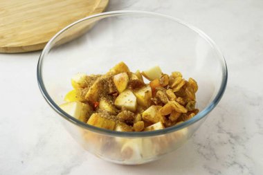 Derin bir kasede, kabak, elma ve kuru üzümleri karıştır. Limon suyu, şeker kamışı ve tarçın ekle. Karıştır.