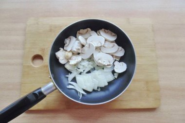 Soğan, sarımsak ve mantar soy ve yıka. Ondan sonra soğanı yarım halkalara, sarımsağa ve mantarları tabaklara ayır. Bir tavaya yerleştir.