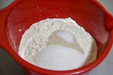 Hamur yoğurmak için bir kabın içinde, kuru malzemeleri karıştır: un, maya, 100 gram şeker, tuz.