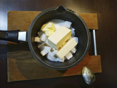 Noel Zencefilli Çörek Evi için gerekli tüm malzemeleri hazırlayın. Hamur yapmaya başlayalım. Bal, tereyağı ve şekeri derin bir kasede karıştır ve ateşe ver. Şeker ve bal tamamen eriyene kadar pişir..