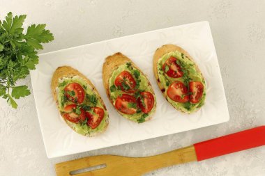 Avokado ve kiraz domatesli lezzetli ve sağlıklı bir sandviç daha her bayram masasını süsleyecek. Çatalla yarım avokado püresi püresi, tadı için limon suyu, tuz ve karabiber ekle. Karıştır. Ekmeği tavada kurut ya da kızart, t ile fırçala