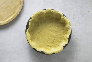 Hamurun yarısını düz bir zeminde yuvarla. Fırın kabına transfer et. Kenarları kenarlara bastır. Pastanın altını delmek için çatal kullan..