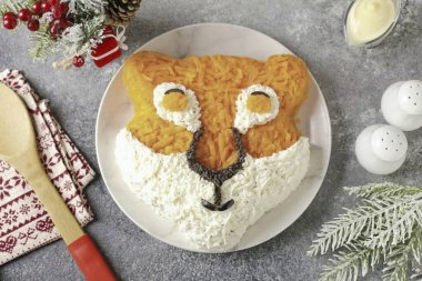 İyi rendelenmiş zeytinleri rendele. Burnu zeytinlerle şekillendirin. Bir ya da iki zeytin dilimini kes, fotoğraftaki gibi göz ve ağız hatlarını çiz. Gözbebeklerini rendelenmiş havuçlarla şekillendir..