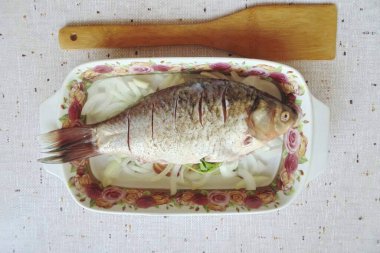 İçinde ve dışında tuzlu balık, biber. Maydanozu içine koy ve haçlı sazanı soğanın üzerine koy. Sırtında küçük çentikler açmak için keskin bir bıçak kullan. Sazanı ayçiçeği yağıyla fırçala ve soğanın üzerine dök..