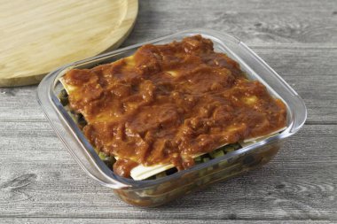 Üst tabaka domates sosu olmalı. Üzerine rendelenmiş peynir serp. Kutuyu folyoyla kapla ve 30 dakika pişir. Sonra folyoyu çıkar ve 10-15 dakika daha pişir..