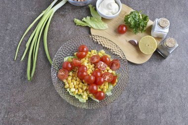 Mısır ekleyin, salamurayı önceden kurutun. Kiraz domateslerini ikiye böl ve salataya ekle..