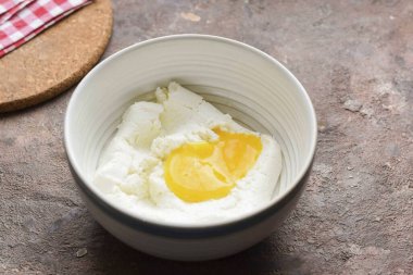 Süzme peyniri bir kaseye koy ve tavuk yumurtası ekle..
