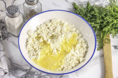 Süzme peyniri derin bir kaba koy ve tuz ekle. Tavuk yumurtasını ayrı bir kabın içinde çırp ve peynirli kekleri yağlamak için kütlenin ayrı bir kısmını ayır. Kalanını kaymağa dök. Her şeyi iyice karıştır, süzme peyniri yoğur.